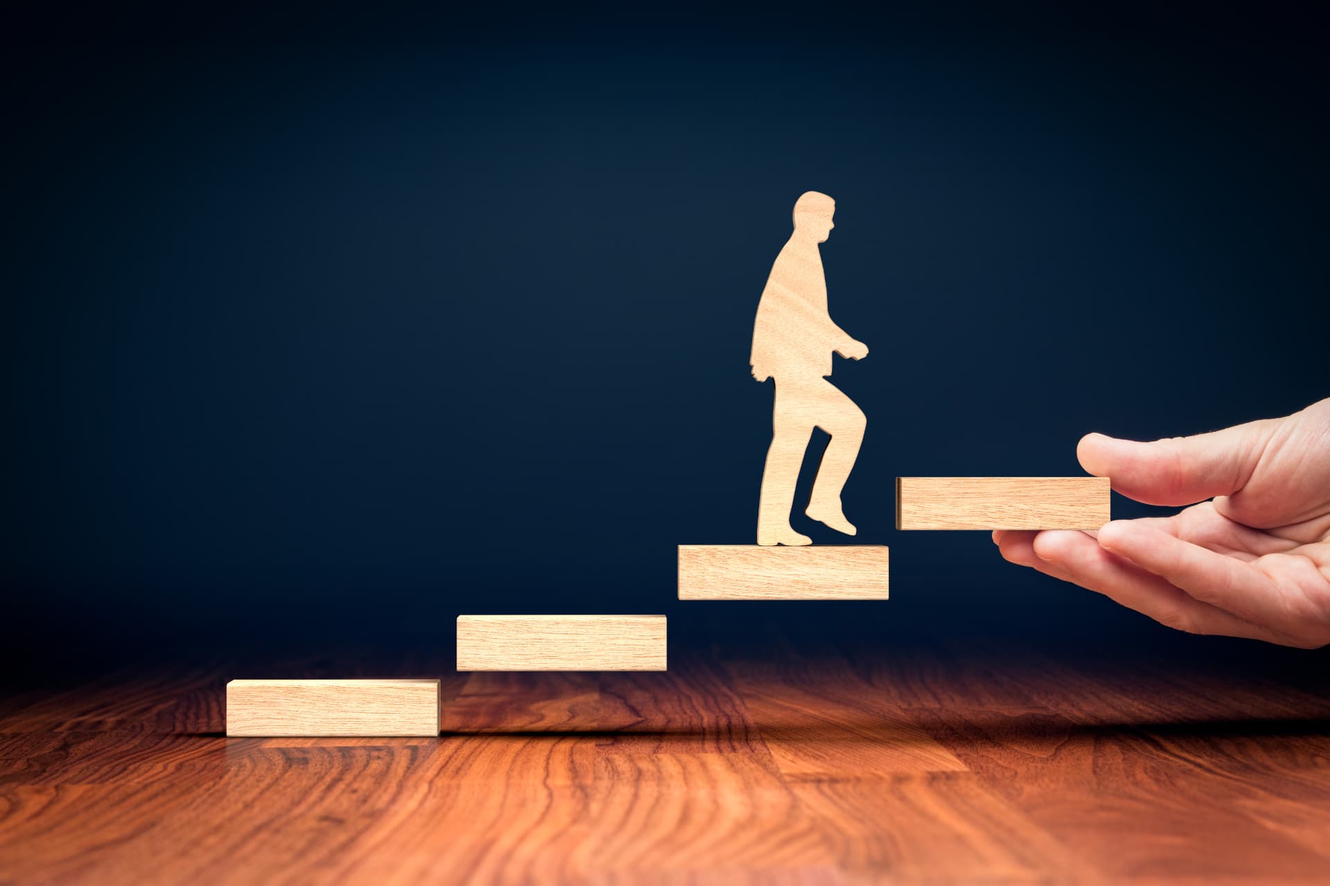 A hand placing the next wooden step for a figure climbing upward
